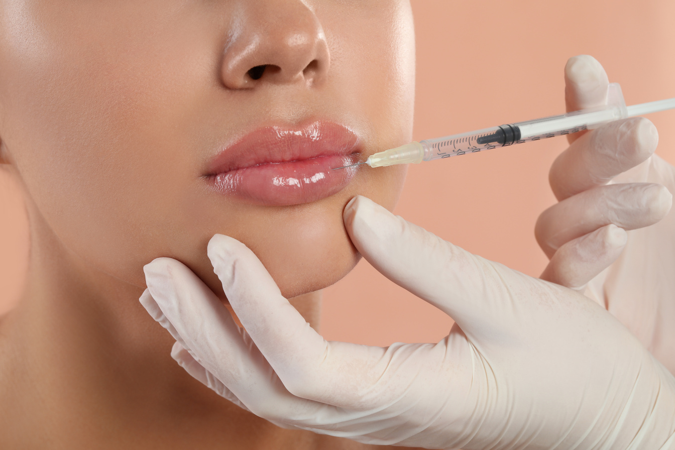 Young Woman Getting Lips Injection on Peach Background, Closeup